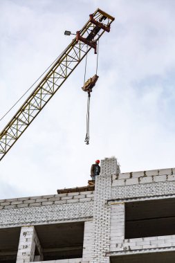 İnşaat halindeki beyaz tuğlalı bir evin çatısında ve gökyüzüne karşı bir vinç. Dikey yönelim.