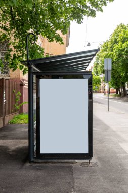 Şehirdeki bir tramvay durağında, ağaçların arkasında duran büyük beyaz bir reklam pankartı. Dikey yönelim.