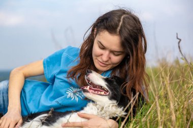 Mavi tişörtlü, siyah beyaz bir köpekli bir kız çimlerin üzerinde uzanıyor ve sarılıyor. Gözleri kapalı bir kız. Yakın plan portre. Yatay yönelim. 