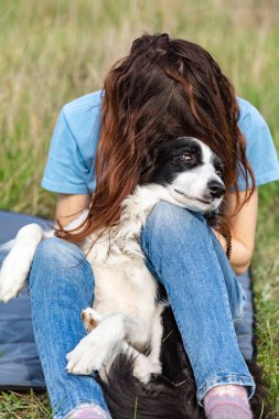 Kız, köpeğini uzun saçlarıyla örten bir çoban köpeğine sarılıyor. Bulanık çimen arka planı. Dikey yönelim. 