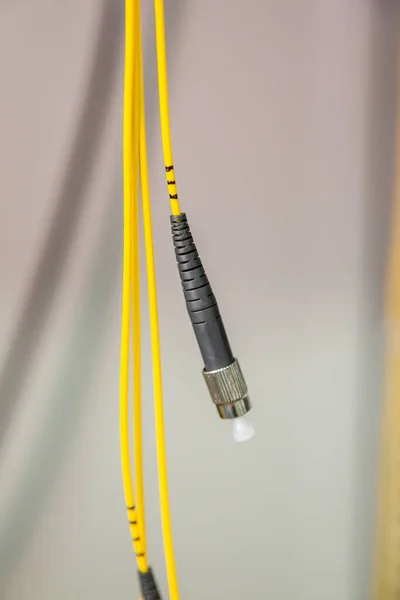 На светлом фоне висит желтый и черный волоконно-оптический кабель с пластиковой прокладкой. Вертикальная ориентация. — стоковое фото