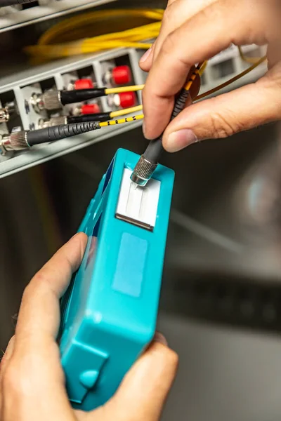 Egy férfi speciális kék tisztítóval tisztítja meg a száloptikás kábeleket. A csatlakozók tisztítása a hálózati kapcsoló hátterének ütközik. Függőleges irány. — Stock Fotó