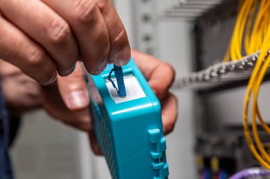Bir adam dolabın yanındaki mavi fiber optik bağlantı temizleyicisiyle çalışıyor. Temizlik konnektörleri kapanıyor. Yatay yönelim.