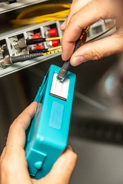 Egy férfi speciális kék tisztítóval tisztítja meg a száloptikás kábeleket. A csatlakozók tisztítása a hálózati kapcsoló hátterének ütközik. Függőleges irány. — Stock Fotó