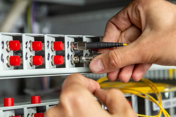 A man inserts a yellow black fiber optic cable into a switch. Hands close up. Horizontal orientation.