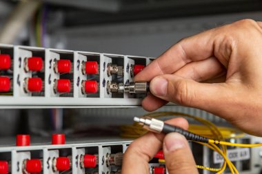 Bir adam düğmeye sarı siyah fiber optik kablo yerleştiriyor. Eller yukarı. Yatay yönelim. 