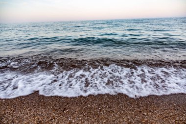 Deniz dalgası küçük çakıl taşlarını kıyıya vurur. Akşam ufkunda deniz. Yatay yönelim.
