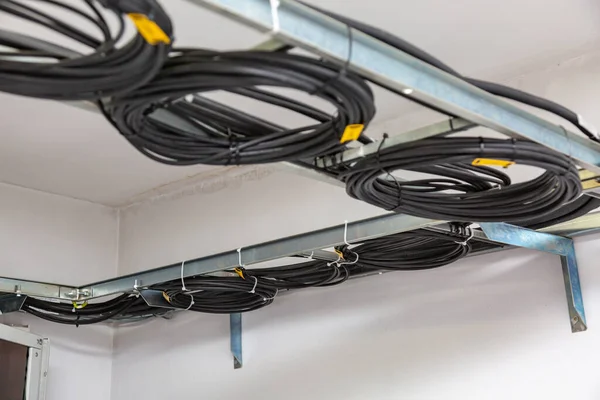 Cable management. Working wires, black cables wound into a coil, a circle. Rings of coiled wires, wire roll on cable ladder on the ceiling. Horizontal orientation.