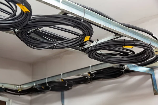 Kabelmanagement. Arbeitsdrähte, schwarze Kabel, die zu einer Spule, einem Kreis, gewickelt sind. Ringe aus gewickelten Drähten, Drahtrollen auf Kabelleitern an der Decke. Horizontale Orientierung. — Stockfoto