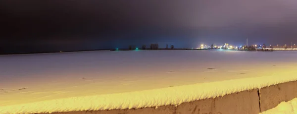 Snow-covered reservoir and parapet in winter at night and station lights on the horizon. Horizontal orientation. High quality photo — Stock Photo, Image