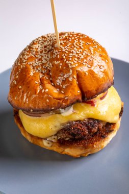 Bol peynirli ev yapımı çizburger, susam tohumlu çörek beyaz arka planda gri bir tabakta. Dikey oryantasyon. Yüksek kalite fotoğraf