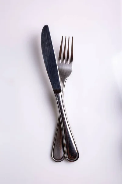 Bestick kniv och gaffel ligger korsade på en vit bakgrund. Utsikt uppifrån. Vertikal orientering. Högkvalitativt foto — Stockfoto