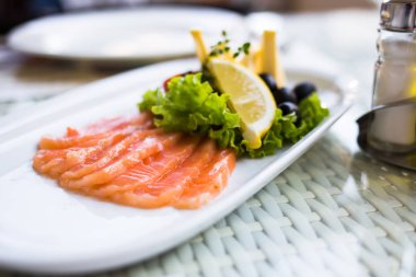 Beyaz plaka üzerinde limon dilimleri ile servis somon füme dilimlenmiş.