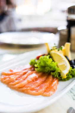 Beyaz plaka üzerinde limon dilimleri ile servis somon füme dilimlenmiş.