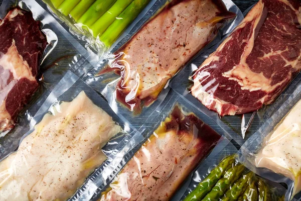 Duck breast, chicken breast, beef steak and asparagus vacuum sealed ready for sous vide cooking, on black background, top view