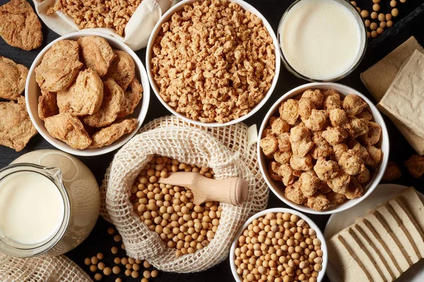 Soy products: soy beans, soy milk, tofu and soya chunks on black background, top view