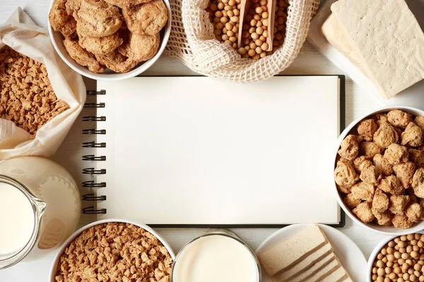 Soy products: soy beans, soy milk, tofu and soya chunks and notebook for copy space on black background, top view