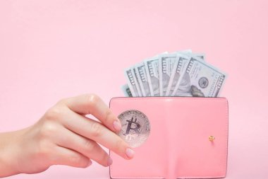 Dolar ve bitcoin kopya alanı ile pembe bir arka plan üzerinde kadının elinde pembe cüzdan