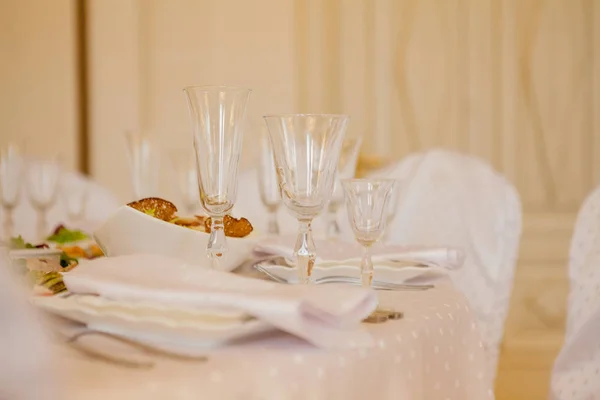 Glasses, flowers, fork, knife, napkin folded in a pyramid, served for dinner in restaurant with cozy interior. Wedding decorations and items for food, arranged by the catering service on a large table