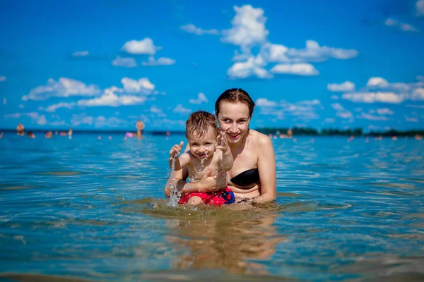 Ibu muda dengan anak laki-laki bermain dengan air di danau di musim panas, kebahagiaan keluarga, istirahat keluarga desa, musim panas hangat hari, kebahagiaan Stok Gambar