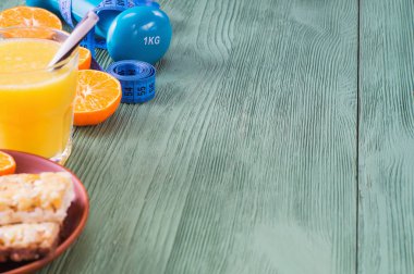 Kopya alanı ile sağlıklı yaşam kavramı. Portakal suyu, meyve. Mısır gevreği barlar, halter ve yeşil ahşap masa kasette ölçme. Tahıl ve meyve - diyet ve Kahvaltı