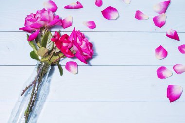 Mavi ahşap arka plan üzerinde bir vazoda pembe gül. Tebrik kartı kavramı. Düğün davetiyesi.