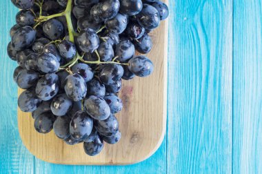 Üzüm mavi ahşap bir masa üzerinde. Dal taze Olgun kırmızı üzüm. Güzel arka plan mavi üzüm bir dalı ile. Koyu kırmızı şarap üzüm. Sağlıklı gıda arka plan. Yaz meyve.