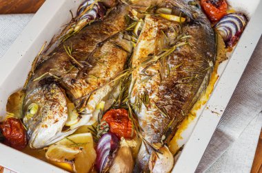 İki lezzetli tamamen pişmiş balık. Pişmiş dorado limon, soğan, biberiye, kiraz domates ve baharat ahşap arka plan üzerinde. Delicious dorado fırın tepsisinde kavrulmuş. Diyet ve sağlıklı gıda. Üstten görünüm.