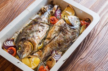 İki lezzetli tamamen pişmiş balık. Pişmiş dorado limon, soğan, biberiye, kiraz domates ve baharat ahşap arka plan üzerinde. Delicious dorado fırın tepsisinde kavrulmuş. Diyet ve sağlıklı gıda. Üstten görünüm.