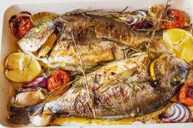 İki lezzetli tamamen pişmiş balık. Pişmiş dorado limon, soğan, biberiye, kiraz domates ve baharat ahşap arka plan üzerinde. Delicious dorado fırın tepsisinde kavrulmuş. Diyet ve sağlıklı gıda. Üstten görünüm.