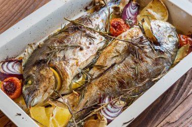 İki lezzetli tamamen pişmiş balık. Pişmiş dorado limon, soğan, biberiye, kiraz domates ve baharat ahşap arka plan üzerinde. Delicious dorado fırın tepsisinde kavrulmuş. Diyet ve sağlıklı gıda. Üstten görünüm.