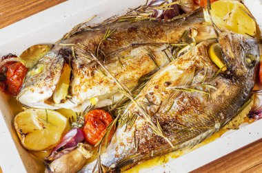 İki lezzetli tamamen pişmiş balık. Pişmiş dorado limon, soğan, biberiye, kiraz domates ve baharat ahşap arka plan üzerinde. Delicious dorado fırın tepsisinde kavrulmuş. Diyet ve sağlıklı gıda. Üstten görünüm.