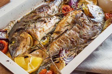 İki lezzetli tamamen pişmiş balık. Pişmiş dorado limon, soğan, biberiye, kiraz domates ve baharat ahşap arka plan üzerinde. Delicious dorado fırın tepsisinde kavrulmuş. Diyet ve sağlıklı gıda. Üstten görünüm.