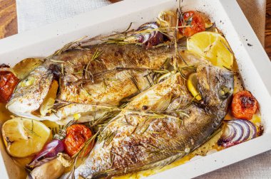 İki lezzetli tamamen pişmiş balık. Pişmiş dorado limon, soğan, biberiye, kiraz domates ve baharat ahşap arka plan üzerinde. Delicious dorado fırın tepsisinde kavrulmuş. Diyet ve sağlıklı gıda. Üstten görünüm.