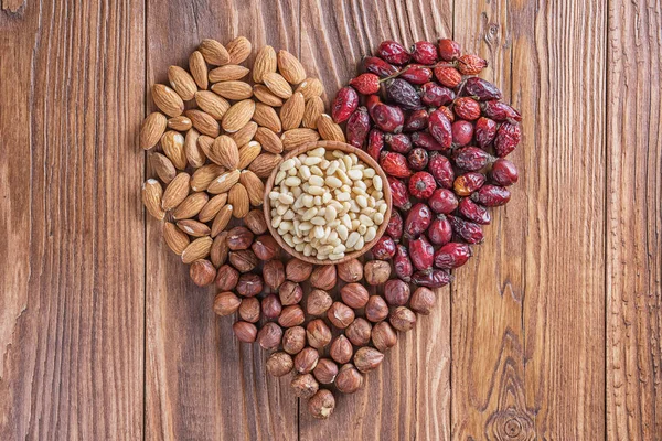 Heart of nuts and dried rose hips on wooden background. Almonds, hazelnuts, pine nuts and dried hips.  The concept of a healthy lifestyle.