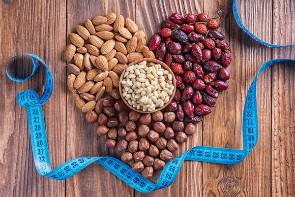 Heart of nuts, dried rose hips and measuring tape on wooden background. Almonds, hazelnuts, pine nuts and dried hips.  The concept of a healthy lifestyle.