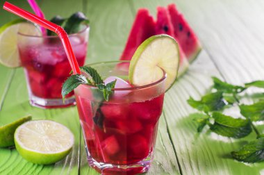 Karpuz karpuz, limon, nane ve buz, kavun mojito dilimleri ile iki kadeh kokteyl. Karpuz ve yeşil ahşap masa üzerinde kırmızı şeritli saman ile ev yapımı limonata. Yaz içeceği.