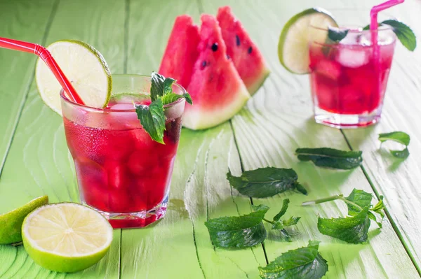 西瓜鸡尾酒两杯 配上西瓜片 薄荷和冰 瓜莫吉托 自制柠檬水与西瓜和红色条纹秸秆在绿色的木桌上 夏季饮品 — 图库照片
