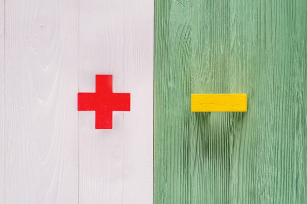 The concept of opposites, plus and minus on white and green wooden board, flat lay. Wooden figures  on a wooden background. Plus versus minus with copy space, top view.