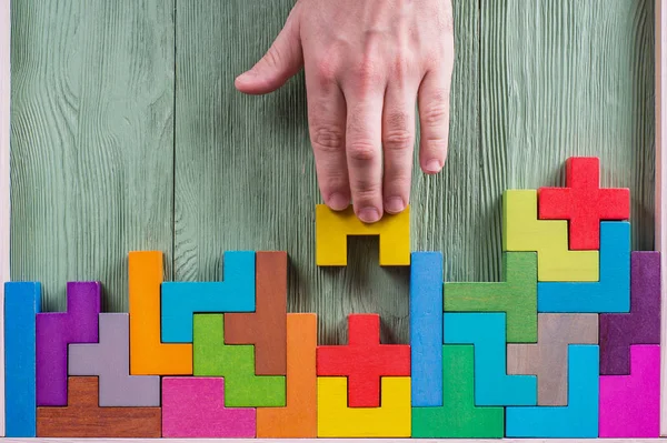 Concept of decision making process, logical thinking. Logical tasks. Conundrum, find the missing piece of the proposed. Hand holding puzzle element. Background with colorful shapes wooden blocks