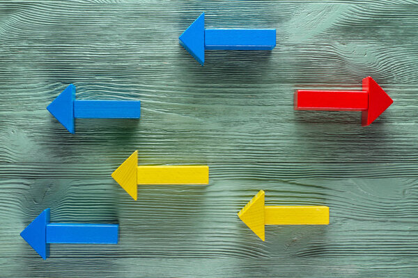 Wooden arrows on wooden background, one arrow in opposite direction from others. The concept of independent thinking, individuality, uniqueness. Business concept, another way.