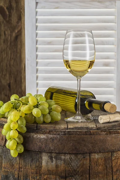 垂直方向の木製樽で白ワインの静物 ワインの瓶 白ワインのガラス 古い木樽にブドウの房 ワインの試飲と生産の概念 — ストック写真