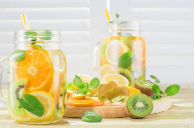 Ahşap masa meyve suyu detoks. Nane ile taze ev yapımı limonata. Yaz bir mason kavanoza bir bambu tabloda narenciye su yenileniyor. Yazlık Ev yapımı kokteyl limon, portakal, kivi ile.