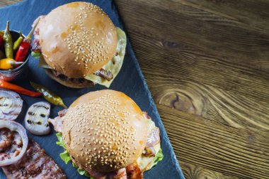 Kopya alanı, üstten görünüm taze lezzetli burger. Kayrak bir rustik ahşap masa gemide iki ev yapımı Hamburger, susam çörek etli sığır köftesi, ızgara soğan, pastırma ve taze salata ile servis. 