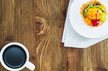 İştah açıcı kek sepeti dilimlenmiş meyve, çilek ve kopya alanı rustik ahşap zemin üzerine kahve. Lezzetli ve taze tatlı ve kahve, üstten görünüm, lay düz. Sabah seçim.