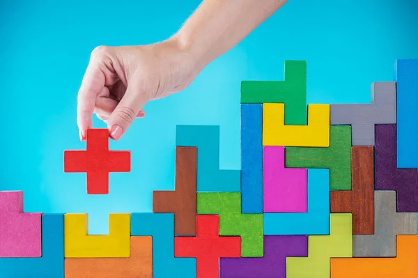 Concept of decision making process, logical thinking. Logical tasks. Conundrum, find the missing piece of the proposed. Hand holding puzzle element. Background with colorful shapes wooden blocks