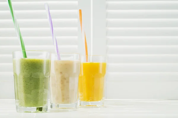 Freshly blended fruit smoothies in glasses on a white wooden background. Fresh fruit cocktails of various colors and tastes, kiwi, banana, orange. Assorted fruit shakes. Diet concept.