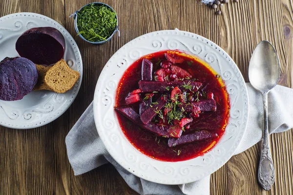 Vegetable soup - red borsch  in a white bowl on a rustic wooden background, top view. Healthy beetroot soup, vegetarian food. Delicious beet soup with croutons, flat lay.