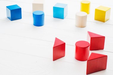 Beyaz ahşap arka plan üzerinde renkli ahşap bloklar. Yaratıcılık oyuncaklar. Çocuk yapı taşları. Geometrik şekiller - küp, üçgen prizma, silindir. Mantıksal düşünme kavramı.