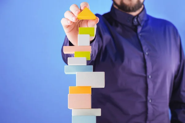 Businessman building tower of colorful wooden blocks. Concept of business success, achievement and self-control.